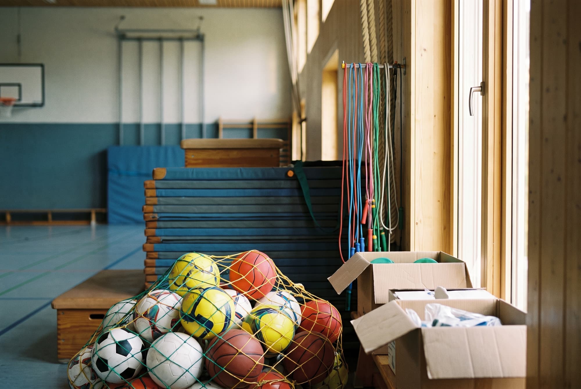 Geräteraum einer Schulsporthalle mit neuen Bällen, Turnmatten und Kartons mit Unterrichtsmaterial